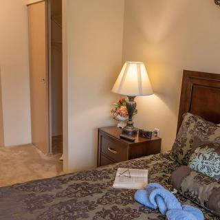 A cozy bedroom featuring a lamp on a nightstand beside a neatly made bed with patterned bedding and a book.