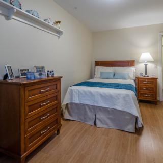A cozy bedroom with wooden furniture and a neatly made bed, featuring a dresser adorned with framed photos.