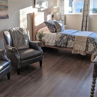 A cozy bedroom with two armchairs, a bed, and sunlight streaming through the window.