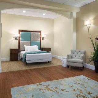 A modern bedroom with a stylish bed, comfortable chair, and decorative elements like a rug and potted plant.