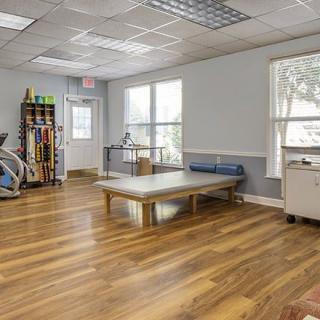 A well-lit physical therapy clinic with exercise equipment and a treatment table.