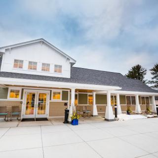 A modern residential building with a spacious porch and a cloudy sky backdrop.