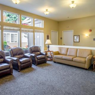 A cozy living room featuring a beige couch, three comfortable chairs, carpeted flooring, and large windows letting in natural light.