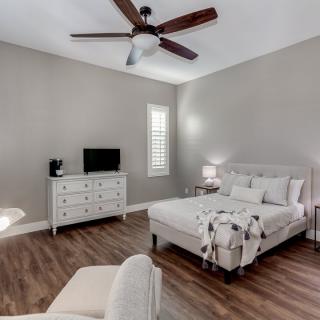 A modern bedroom interior featuring a neatly made bed, dresser with a TV, and a ceiling fan.