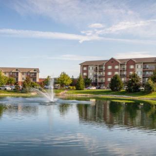 Scenic view of apartment buildings by a lake with a fountain and trees.