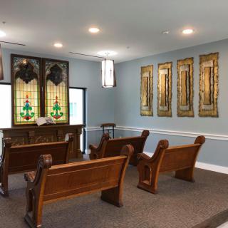 A small chapel interior featuring wooden pews and stained glass windows.
