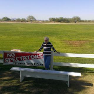 A person stands next to a 'No Spectators' sign in a large open field.