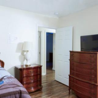 A bedroom featuring a dresser with a television and a bedside table with a lamp.