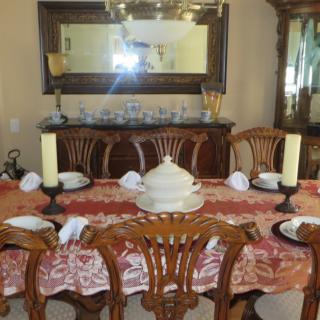 A dining room with a decorated table, featuring an ornate tablecloth, candles, and dinnerware.