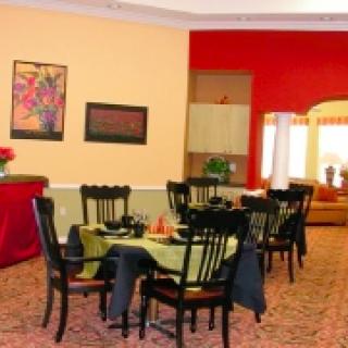 A cozy dining area with neatly arranged tables and chairs, featuring artwork on the walls and a warm color scheme.