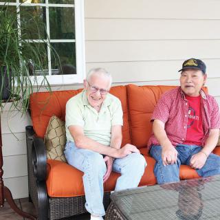 Two people sitting on a couch outside, enjoying a conversation on a patio.