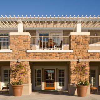 A two-story building with a stone facade, balconies, and a pergola at the top level.