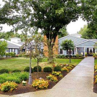 A landscaped garden with a pathway leading to a building, surrounded by trees and flowers.
