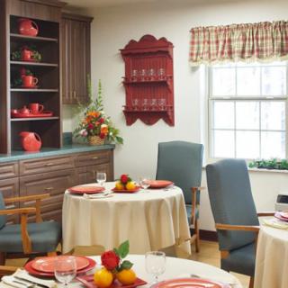 A cozy dining room with tables set for a meal, featuring red accents and warm decor.