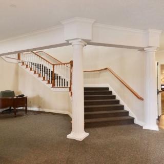 A spacious interior featuring a staircase with wooden banisters and white columns.