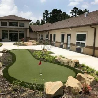 An outdoor mini-golf course next to a building, surrounded by landscaping and greenery.