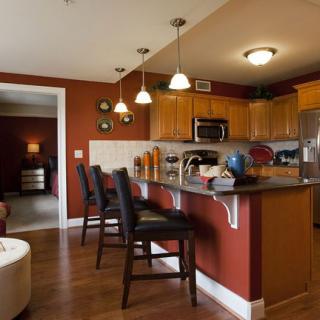 A modern kitchen interior with wooden cabinets and a countertop, featuring bar stools and pendant lighting.