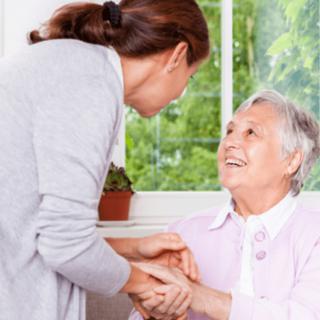A caregiver providing support and companionship to an elderly woman indoors.