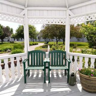 A peaceful gazebo with a green bench overlooks a sunny garden path.