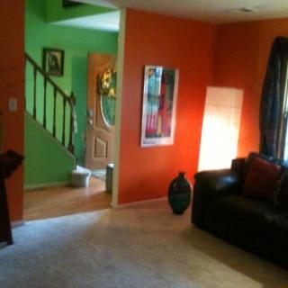 A modern living room with vibrant orange walls and a green hallway.