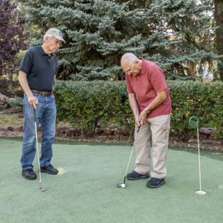 Two elderly men enjoying a game of golf on a putting green.
