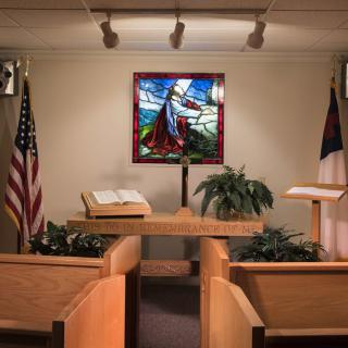 A chapel interior featuring a pulpit with an open Bible, stained glass window, and flags.