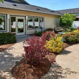 A landscaped garden with various colorful plants and shrubs surrounding a house's patio on a sunny day.