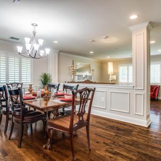 A well-decorated dining room with a wooden floor and chandelier, featuring a large dining table and chairs in an open concept layout.