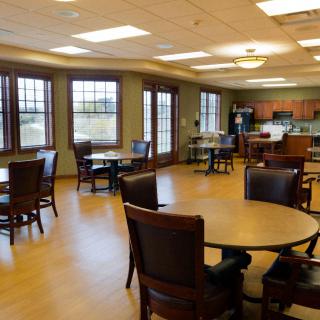 A spacious dining area with multiple tables and chairs, adjacent to a kitchen with large windows providing natural light.