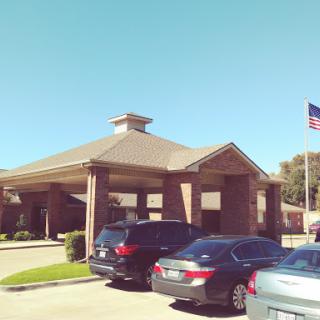 A well-structured building with a flag, surrounded by parked cars on a clear day.