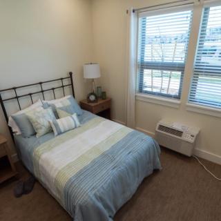 A cozy bedroom with a neatly made bed, nightstand, and window.