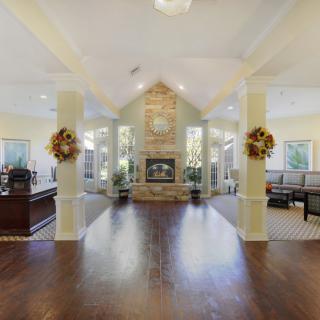 A spacious living room with a central fireplace, featuring hardwood floors, vaulted ceilings, and decorative columns.