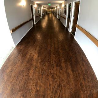 A wide-angle view of a well-lit hallway with wooden flooring and doors on either side.