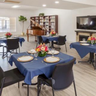 A well-appointed dining area with blue tablecloths, elegantly set tables, and a piano in the background.