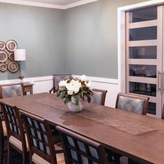 A modern dining room with a long wooden table, surrounded by chairs and decorated with a central flower arrangement and wall decor.