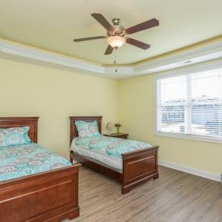 A bright bedroom with two twin beds, a ceiling fan, and a large window.
