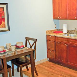 A cozy kitchen and dining area with wooden cabinets, a small table set for two, and wall art.