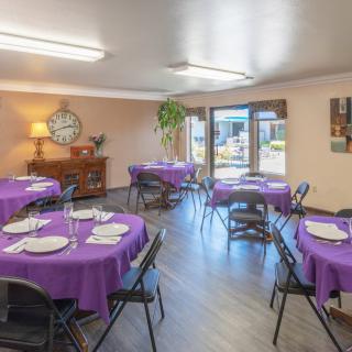 A dining room setup with multiple tables covered in purple tablecloths.