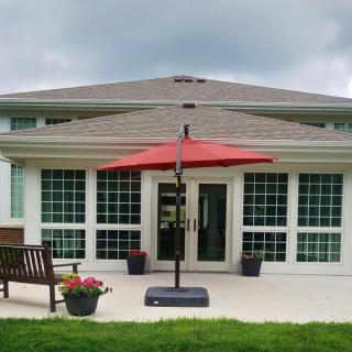 A modern house with a patio featuring a red umbrella, bench, and surrounding garden.