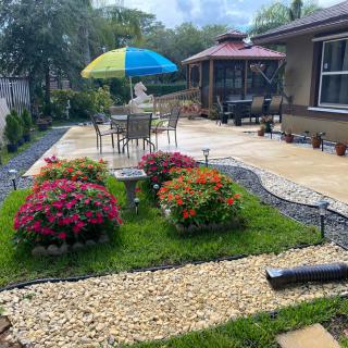 A beautifully landscaped backyard with a patio area, featuring colorful flowers and outdoor seating under an umbrella.