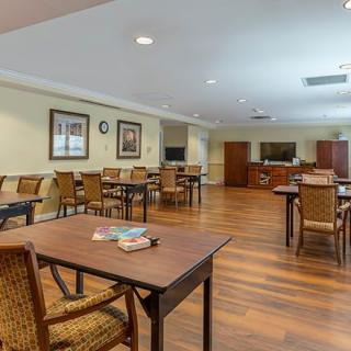 A spacious community dining room with wooden floors and neatly arranged tables and chairs.