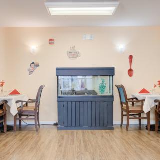 A cozy dining area featuring a central fish tank, surrounded by tables with neatly arranged chairs and decorative wall art.
