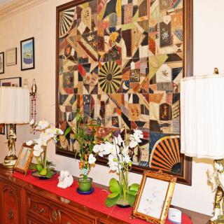 A cozy interior featuring a colorful quilt wall art piece, flanked by elegant lamps and decorated with potted orchids on a wooden cabinet.