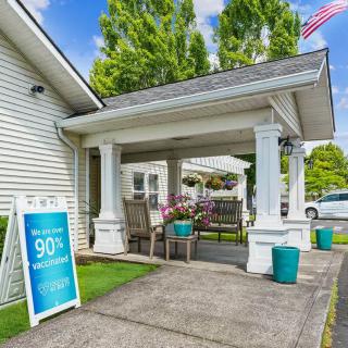 A welcoming entrance with a porch featuring outdoor seating and a signboard, flanked by greenery and an American flag.