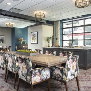 A modern dining room with floral upholstered chairs and a large wooden table, illuminated by stylish chandeliers.