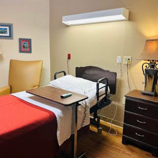 A cozy hospital room with a bed, recliner chair, and bedside table.