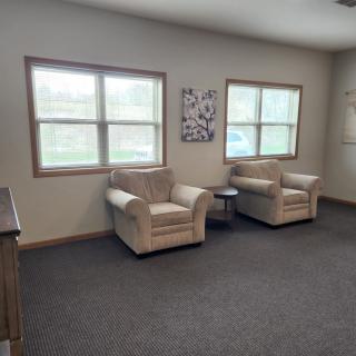 A cozy living room with two armchairs, large windows, and carpeted flooring.