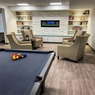 A modern game room featuring a pool table, seating area with armchairs, a wall-mounted television, and built-in bookshelves.