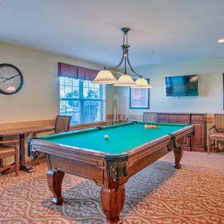 A cozy game room featuring a billiards table under a light fixture, with a television mounted on the wall.