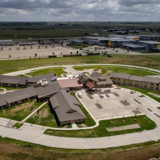 An aerial view of a large building complex with surrounding parking areas and green spaces under a cloudy sky.
